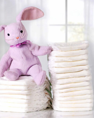 A cute stuffed pink rabbit sitting on a stack of diapers to demonstrates that Center For Women offers baby supplies.